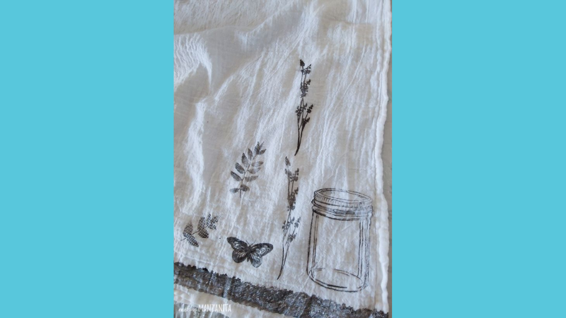 Tea towel with customs stamps in black ink including an empty jar, butterfly, and fern leaves.