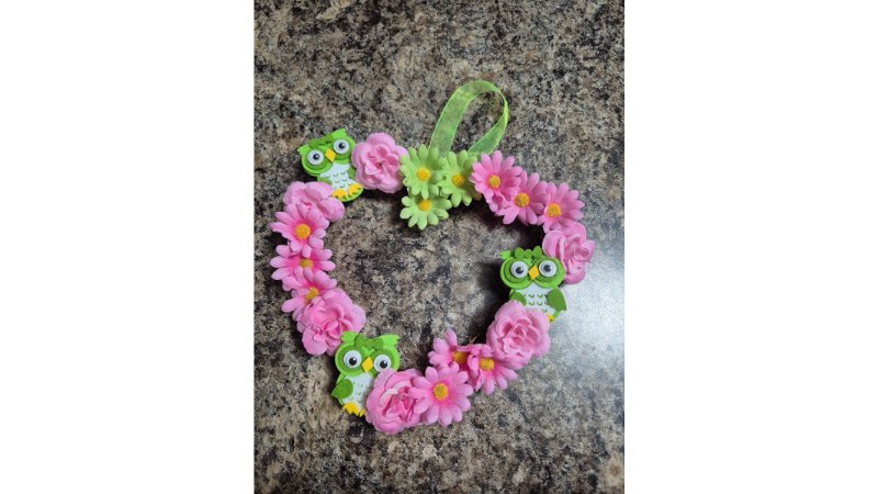 Heart shaped wreath decorated with pink and green fake flowers and green felt owls with a green hanging ribbon